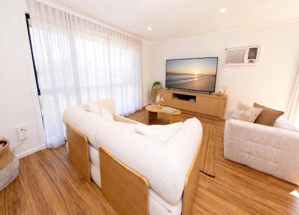 A modern living room with a sofa, a smaller couch, a flat-screen TV, and a wooden floor.