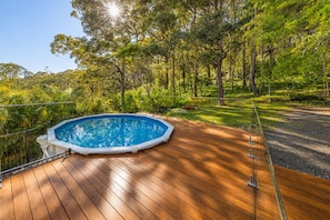 Piscina rectangular sobre una terraza de madera rodeada de exuberante vegetación.