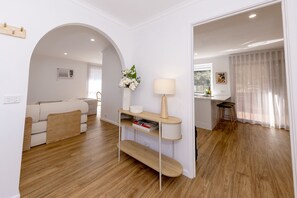 Una sala de estar moderna con un sofá, una mesa de centro y una lámpara. Se ve un área de cocina a través de un arco.