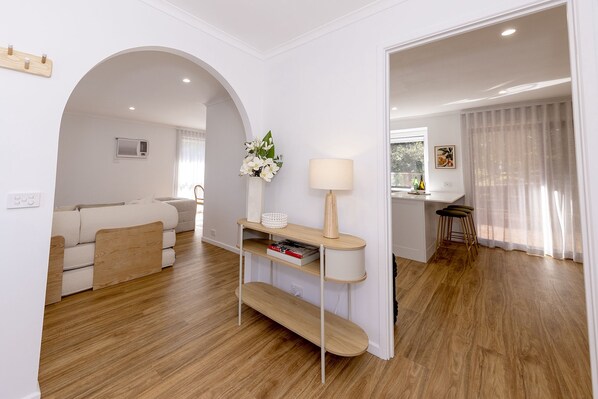 A modern living room with a sofa, a coffee table, and a lamp. There is a kitchen area visible through an archway.
