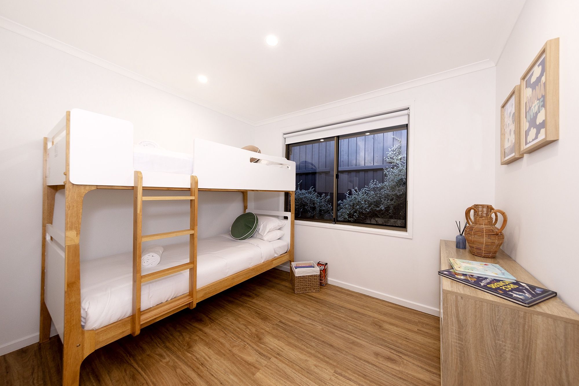 A bunk bed room with a window, a small table with a vase, and a framed picture on the wall.
