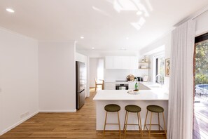 Una cocina moderna con armarios blancos, un refrigerador de acero inoxidable y una zona de bar con taburetes.