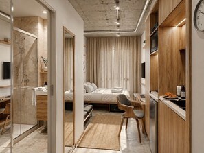 Ein kleines Hotelzimmer mit Bett, Schreibtisch, Stuhl und einer Dusche.