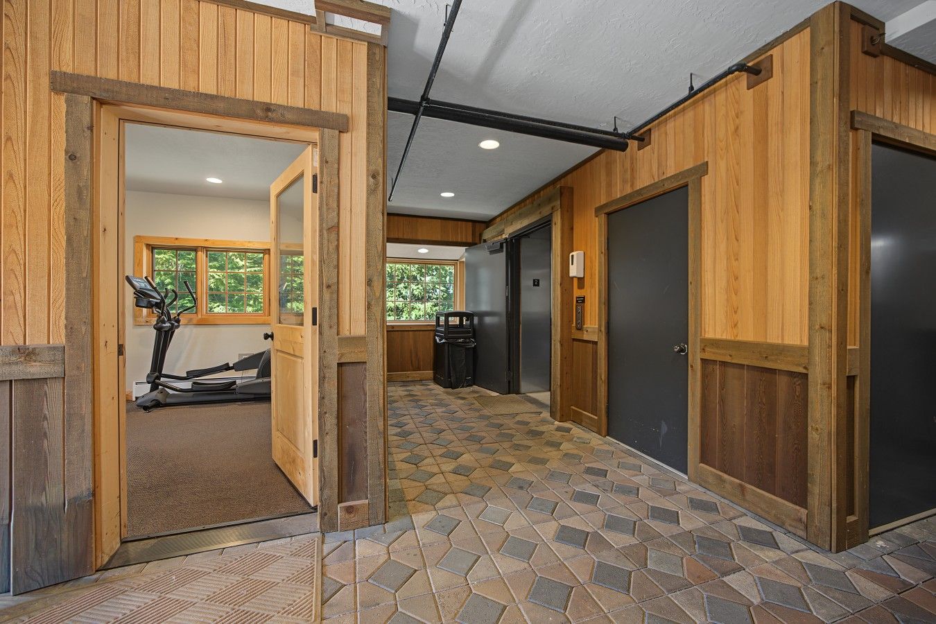 A hallway with wooden walls and a tiled floor leading to a room with a treadmill.