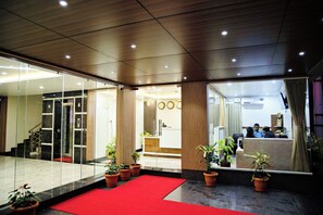 A hotel lobby with a reception desk, a staircase, and potted plants. - Hotel Airstay Inn (Bandikodegehalli Amanikere)