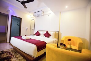 A hotel room with a bed, a chair, a small table with flowers, and an air conditioning unit. - Hotel Airstay Inn (Bandikodegehalli Amanikere)