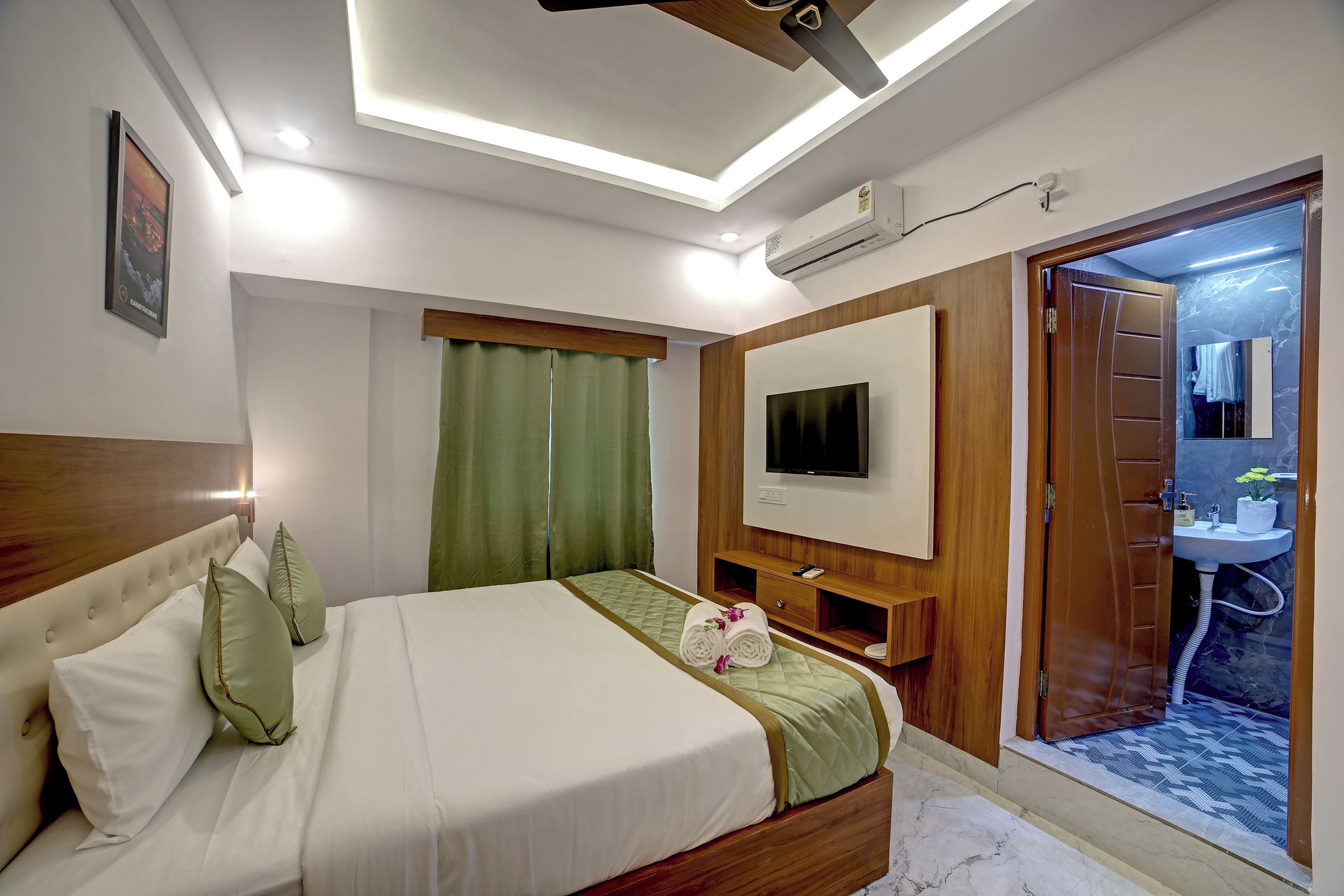 Habitación de hotel con cama, televisor, armario de madera y baño visible a través de una puerta abierta.