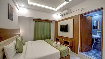 Habitación de hotel con cama, televisor, armario de madera y baño visible a través de una puerta abierta.