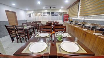 Un comedor con una mesa larga dispuesta para dos personas, rodeada de sillas, con una encimera de cocina y un refrigerador Coca-Cola al fondo.