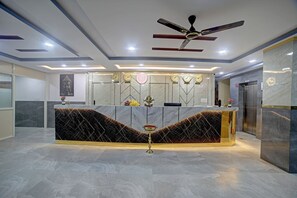 A reception desk with a marble counter, a ceiling fan, and clocks indicating different cities. - Hotel Airstay Inn (Bandikodegehalli Amanikere)