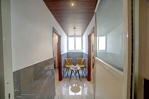A narrow hallway with two chairs and a table, leading to a room with a large window. - Hotel Airstay Inn (Bandikodegehalli Amanikere)