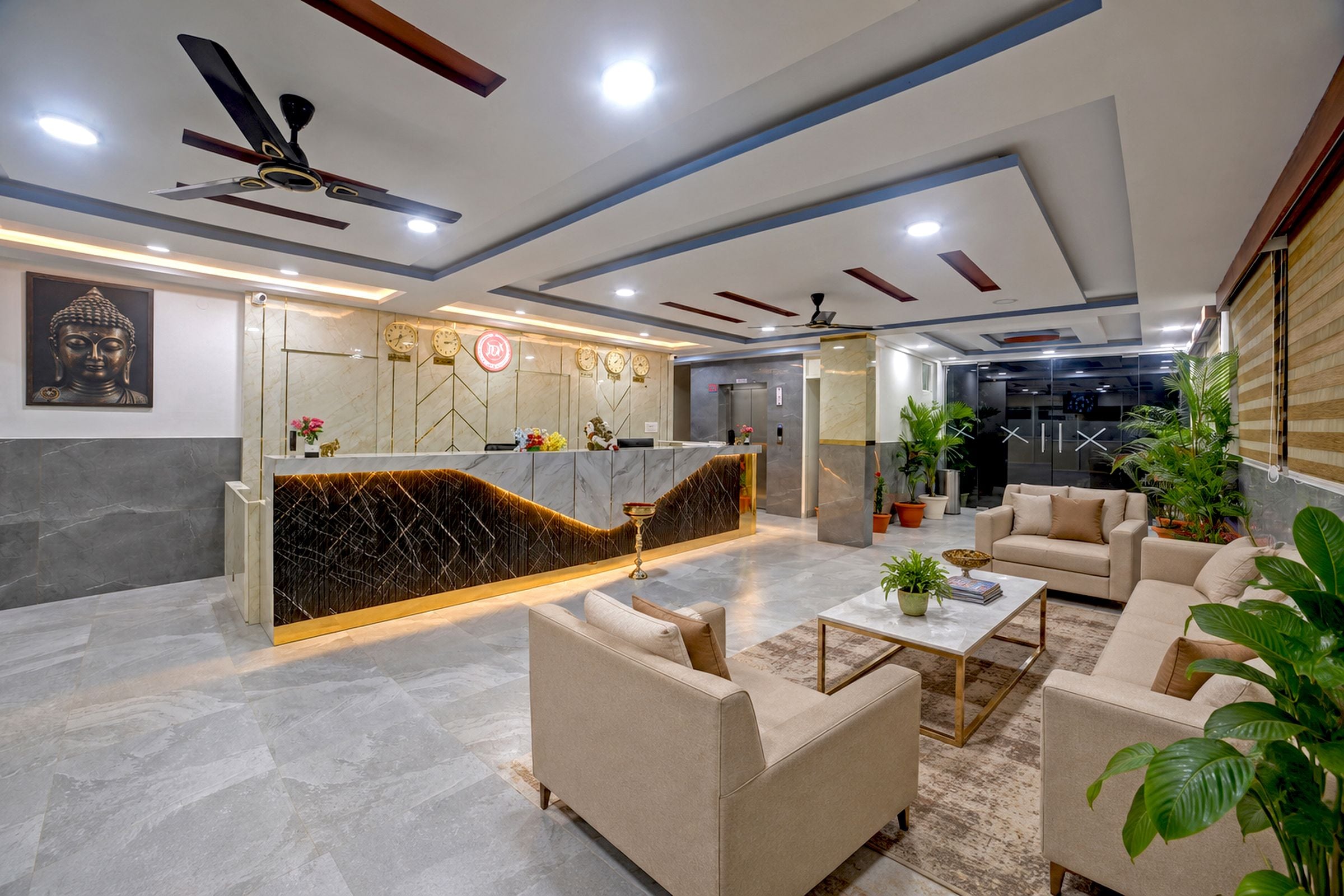 A modern reception area with marble flooring, a reception desk, seating area with sofas, ceiling fans, and a large Buddha statue.