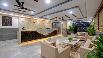 A modern reception area with marble flooring, a reception desk, seating area with sofas, ceiling fans, and a large Buddha statue.