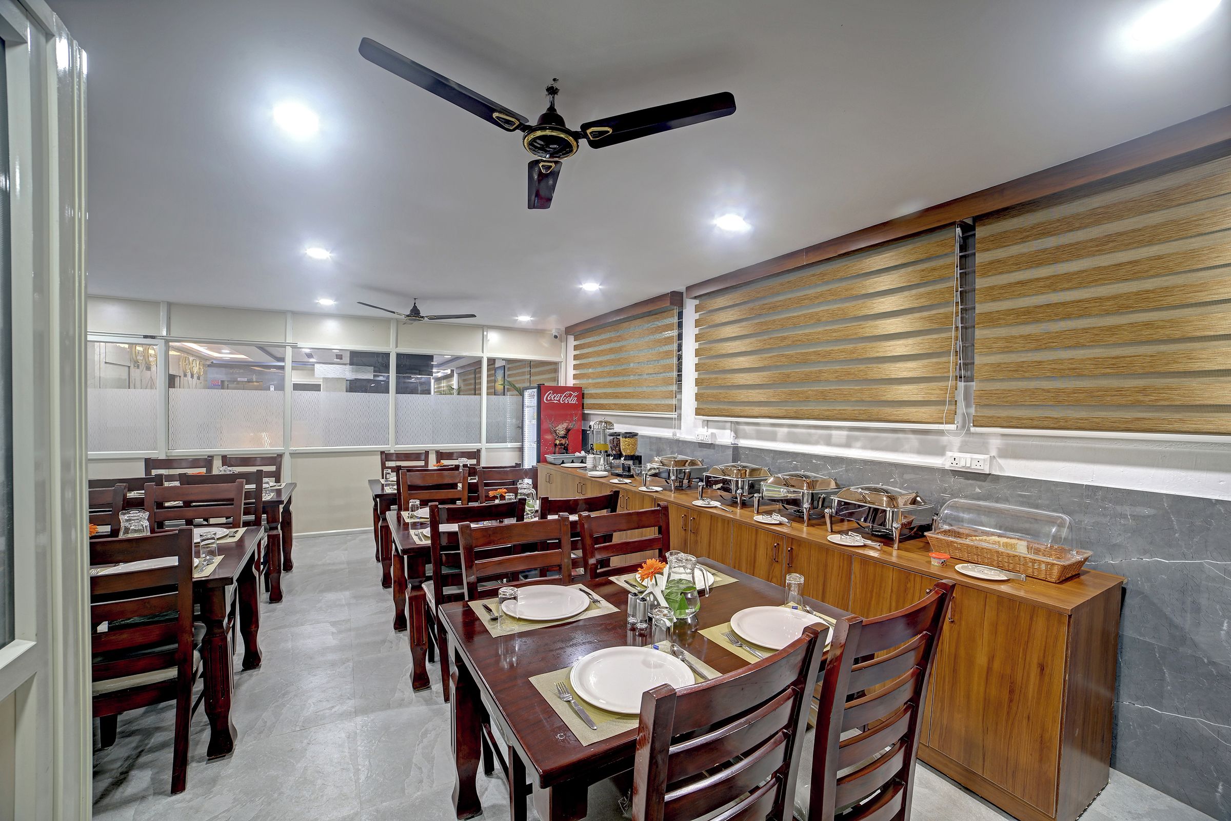 Un área de comedor con mesas y sillas de madera, un mostrador de buffet y un ventilador de techo.