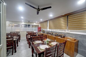 A dining area with wooden tables and chairs, a buffet counter, and a ceiling fan. - Hotel Airstay Inn (Bandikodegehalli Amanikere)