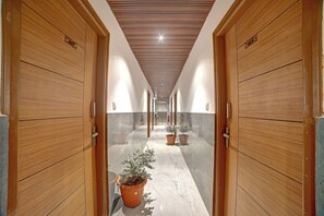A corridor with wooden doors, potted plants, and a tiled floor. - Hotel Airstay Inn (Bandikodegehalli Amanikere)