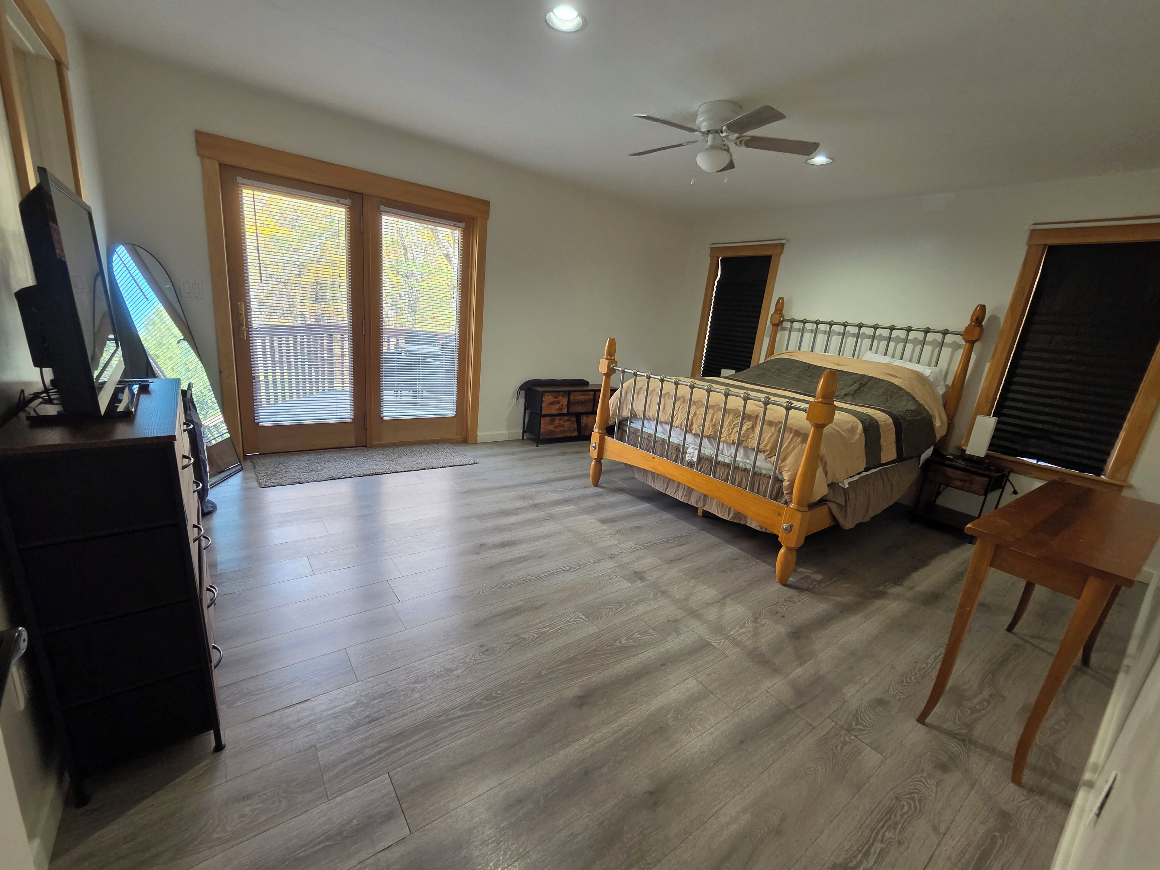 A bedroom with a bed, a desk, a chair, a ceiling fan, and a sliding glass door.