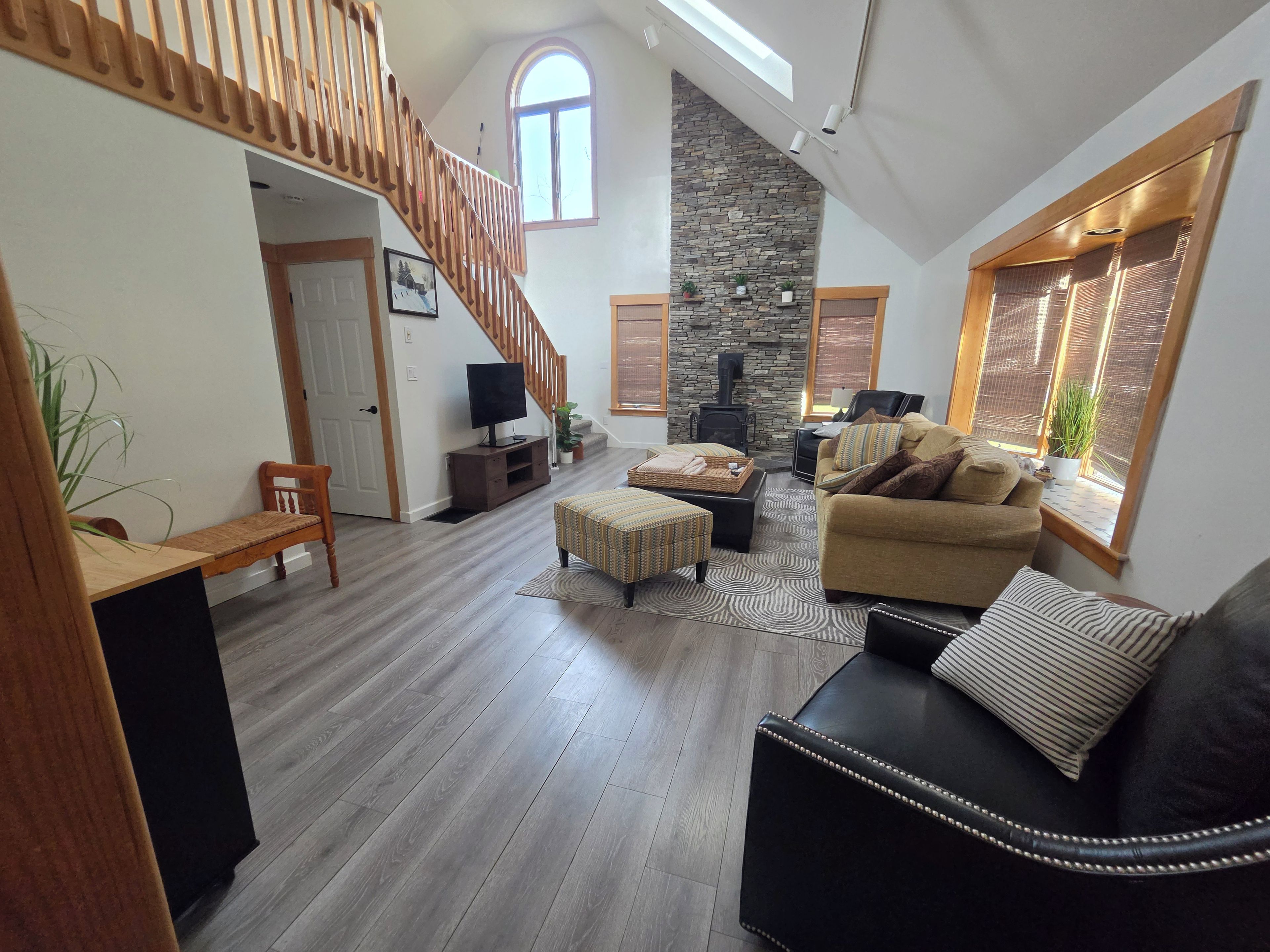 A spacious living area with a wooden staircase, a stone fireplace, and a cozy seating arrangement.