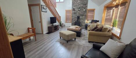 A spacious living area with a wooden staircase, a stone fireplace, and a cozy seating arrangement.