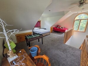 A loft-style room with a bed, a foosball table, and a window with a view of trees.