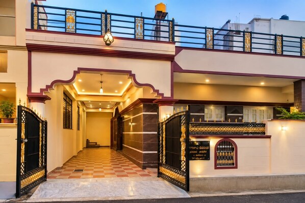 A hotel entrance with a checkered floor, a black gate with gold detailing, and a balcony with a railing.