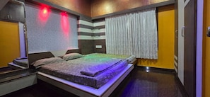 Un dormitorio con cama, mesita de noche, espejo, ventana con cortinas y una puerta.