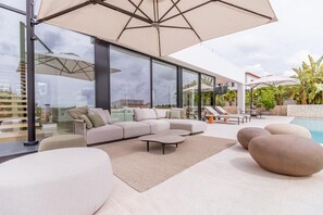 A modern outdoor living area with a sectional sofa, round coffee table, and a pool. - Villa Llum de Mar - Benissa, Costa Blanca (Benissa)