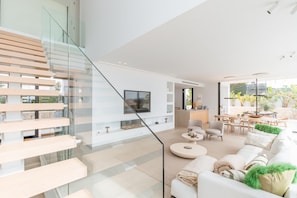 A modern living room with a glass staircase, a flat-screen TV, a dining area, and a view of the outdoors. - Villa Llum de Mar - Benissa, Costa Blanca (Benissa)