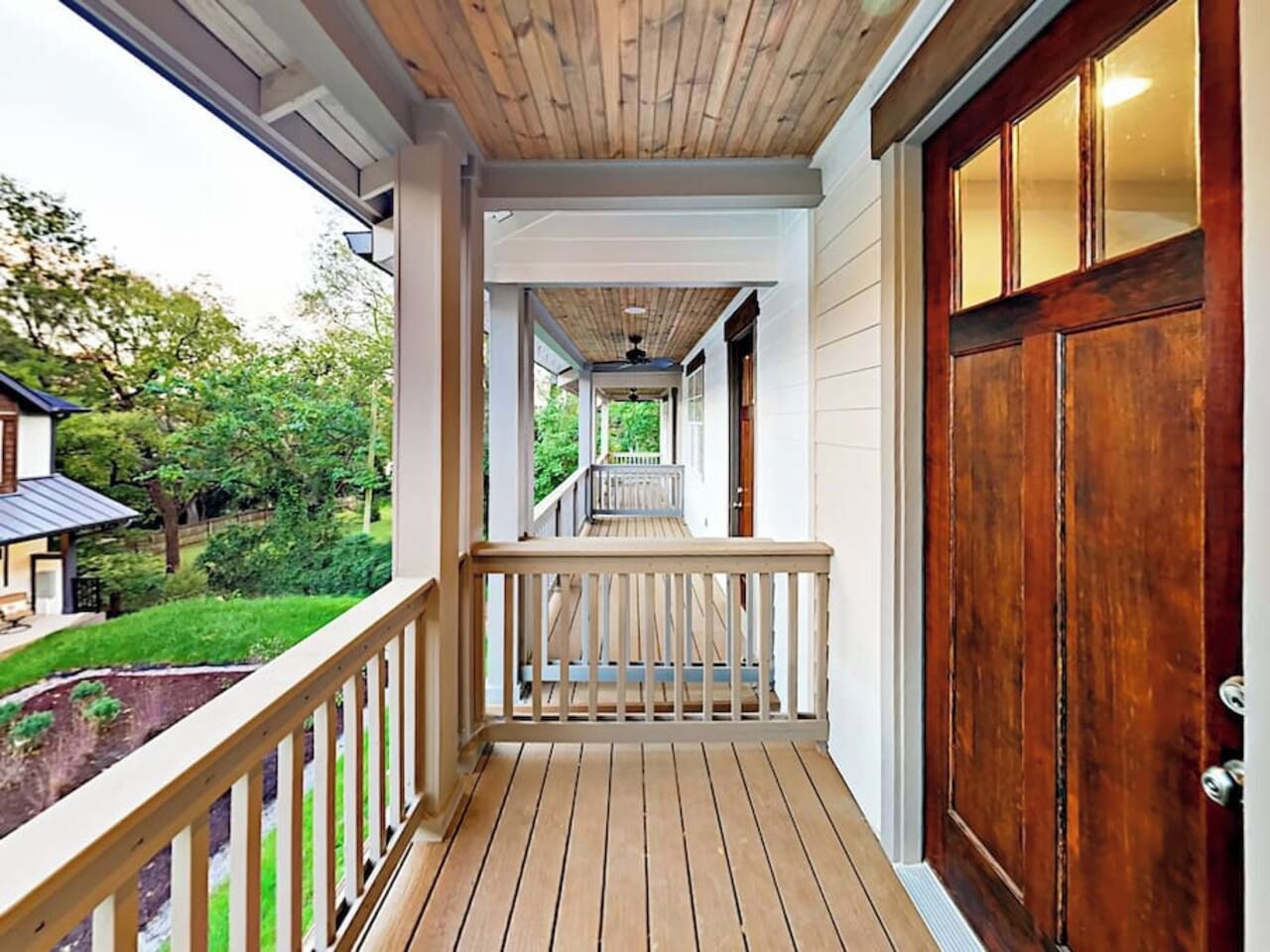 A covered porch with a wooden floor and railing, leading to a door with a glass panel.