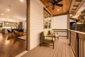Terraza de madera con mobiliario exterior, ventilador de techo y vista del área interior de cocina y comedor.