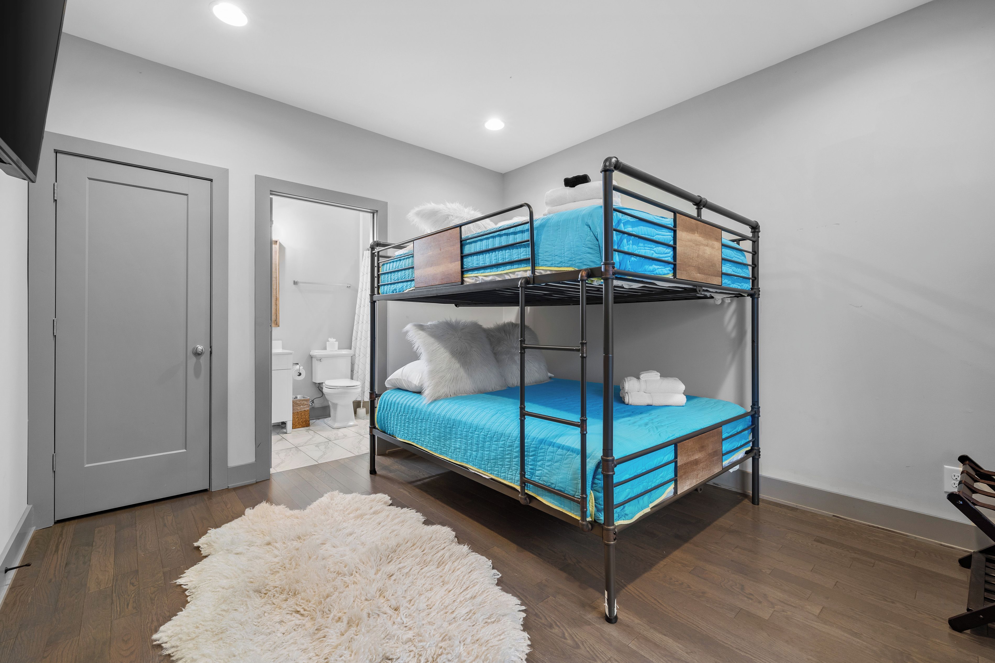 A bunk bed with a blue mattress and white pillows, a fluffy white rug, and a wooden bench.