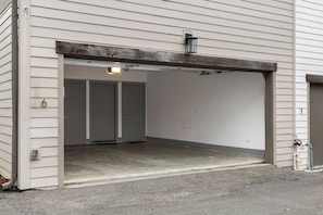 Una entrada de garaje con piso de concreto, estructura metálica de puerta y una luminaria pequeña en el techo.