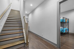 A staircase with wooden steps and metal railings, leading to a room with a bunk bed and a door.