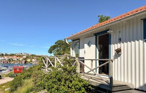 A coastal house with a wooden deck, a view of the marina, and a clear sky. - Beach front home in Kungshamn Hovenäset with sauna (Kungshamn Hovenäset)