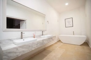 Un baño moderno con dos lavamanos, un espejo grande y una bañera independiente.