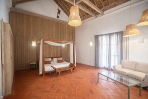 Ein Zimmer mit einem Himmelbett, einem Glastisch, einem weißen Sofa und einem großen Fenster mit Vorhängen.