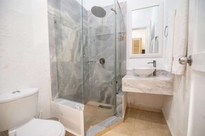 A bathroom with a glass-enclosed shower, a white toilet, a sink with a marble countertop, and a mirror above the sink. - Luxury Room in Casa Escallon (Cartagena)