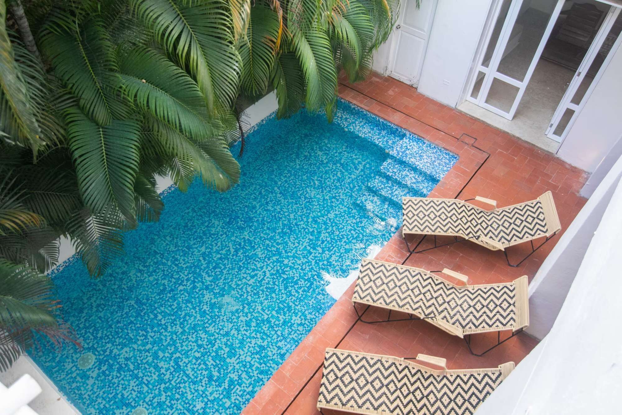 A swimming pool with a patterned tile floor, surrounded by palm trees and a white building.