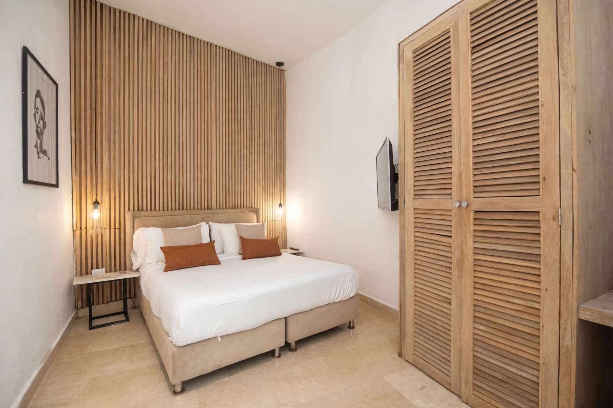 A bedroom with a bed, bedside tables, a wooden wardrobe, and a wall-mounted TV.