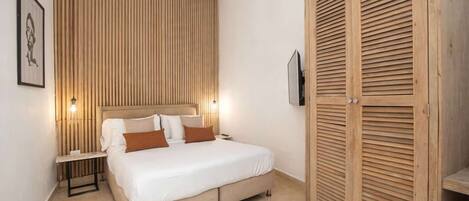 A bedroom with a bed, bedside tables, a wooden wardrobe, and a wall-mounted TV.