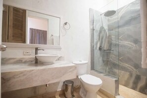 Casa de banho com lavatório de mármore, sanita e cabine de duche com parede de vidro.