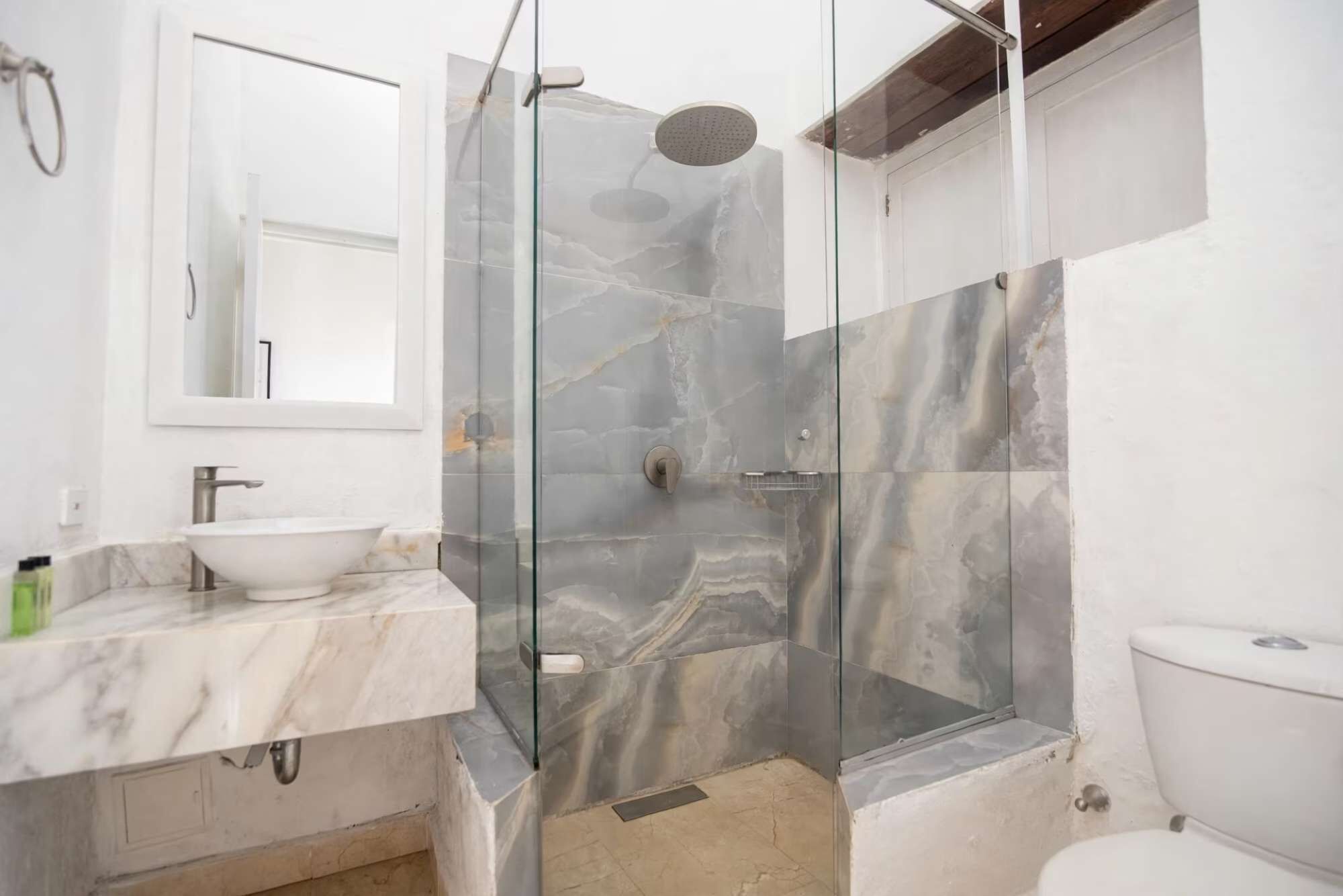 A bathroom with a glass-enclosed shower, a white sink, and a toilet.