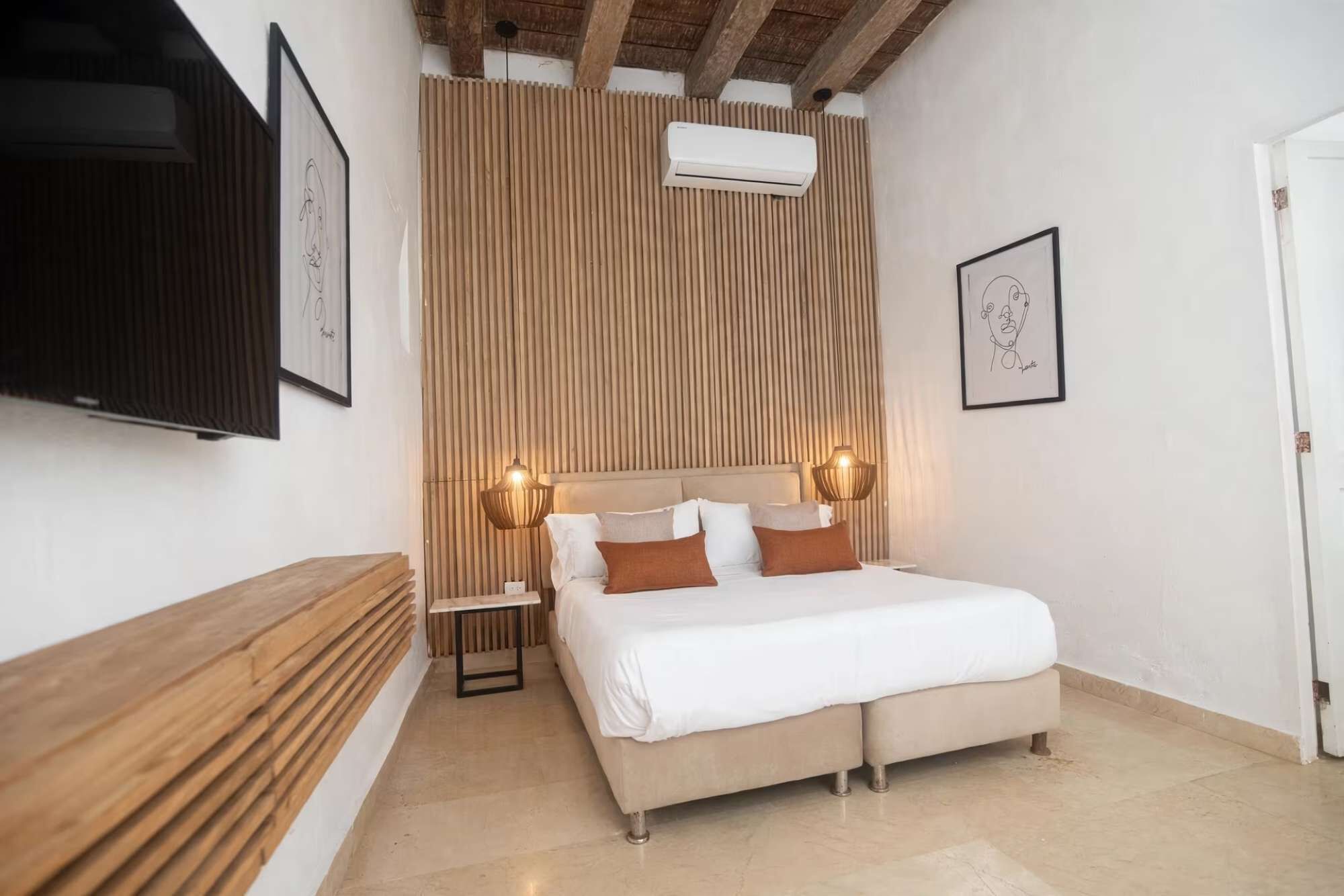 A bedroom with a bed, bedside tables, a wooden slat wall, an air conditioning unit, and framed artwork.