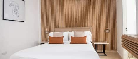 A hotel room with a bed, bedside tables, a wall-mounted air conditioner, and a framed artwork.