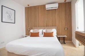 Ein Hotelzimmer mit einem Bett, Nachttischen, einer Wand-Klimaanlage und einem gerahmten Kunstwerk.