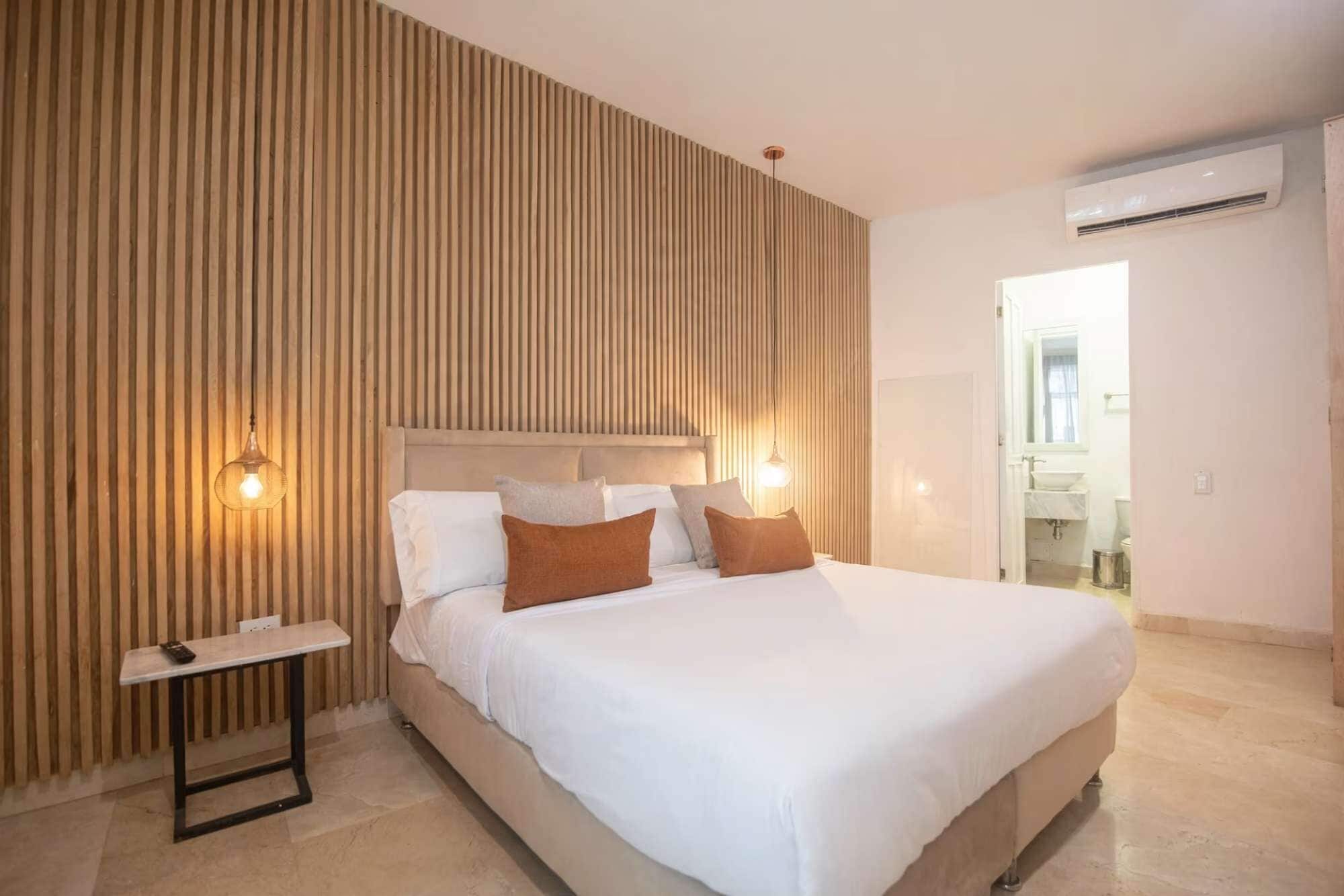 A bedroom with a bed, bedside tables, and a wall-mounted air conditioning unit.