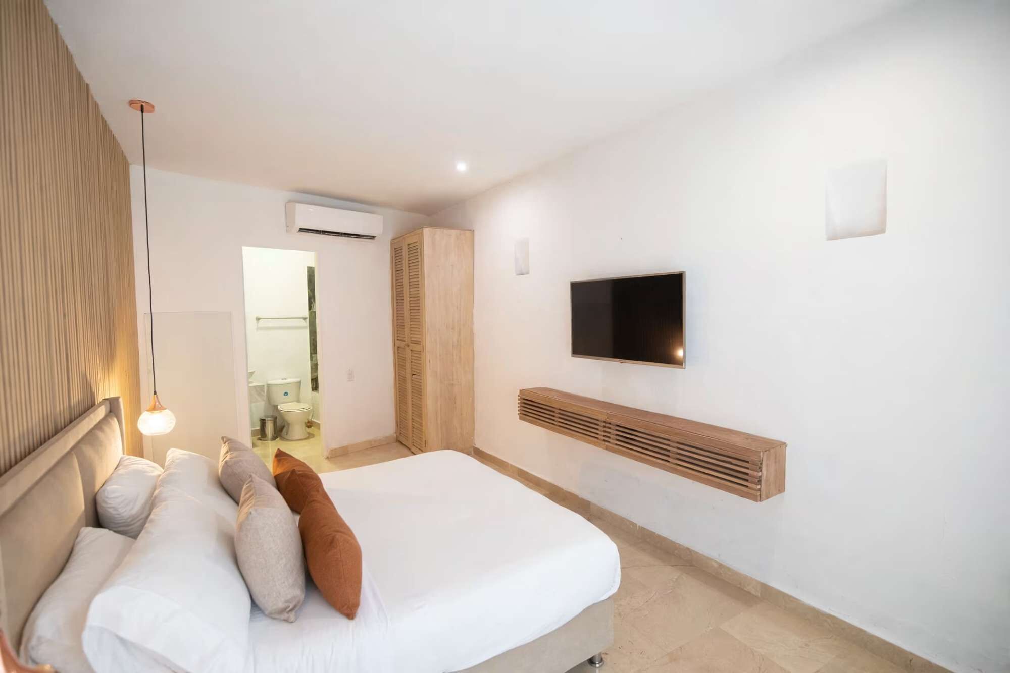 A hotel room with a bed, a television mounted on the wall, and a wooden bench.