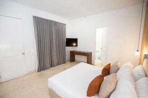 A bedroom with a bed, a TV mounted on the wall, a wooden bench, and a door. - Luxury Room in Casa Escallon (Cartagena)