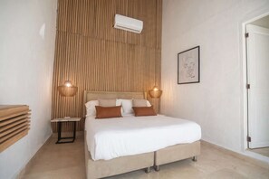A bedroom with a bed, bedside lamps, a wall-mounted air conditioner, and a framed artwork. - Luxury Room in Casa Escallon (Cartagena)