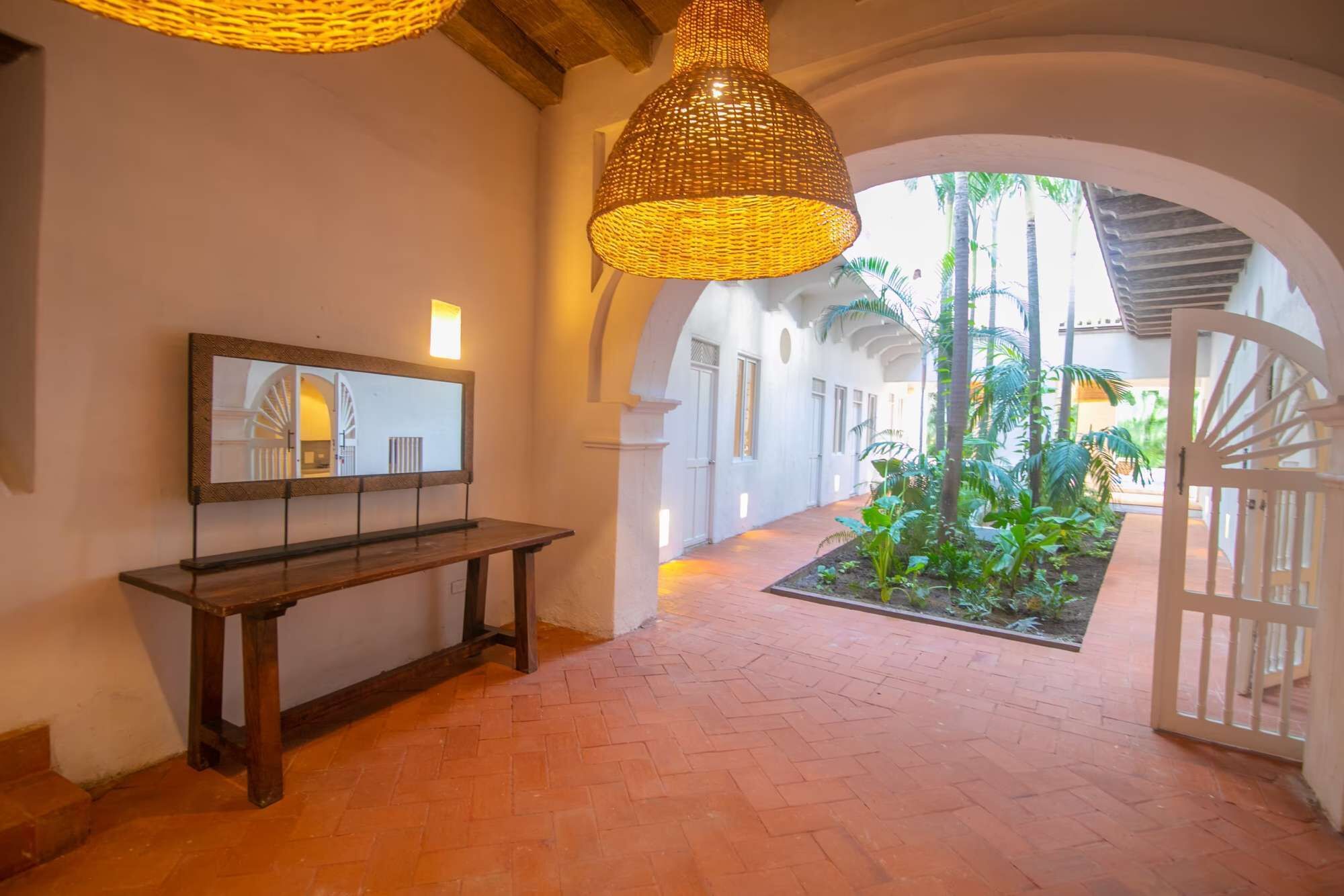 Corredor interno com um banco, luminária pendente e vista para um jardim externo.